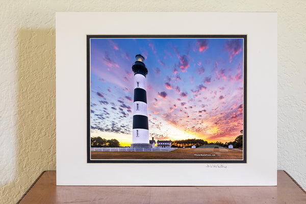 Bodie Island Lighthouse at Sunset: A Beacon Beneath Cotton Candy Skies. This stunning scene captures the magic of the Outer Banks, where history and nature blend seamlessly.
Interesting Facts About Bodie Island Lighthouse:
	1.	Third Time’s the Charm: The current Bodie Island Lighthouse is the third built on this site. The first one was abandoned due to structural issues, and the second was destroyed during the Civil War.
	2.	Height and Reach: Standing at 156 feet, the lighthouse’s first-order Fresnel lens