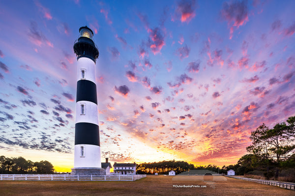 Bodie Island Lighthouse at Sunset: A Beacon Beneath Cotton Candy Skies. This stunning scene captures the magic of the Outer Banks, where history and nature blend seamlessly.
Interesting Facts About Bodie Island Lighthouse:
	1.	Third Time’s the Charm: The current Bodie Island Lighthouse is the third built on this site. The first one was abandoned due to structural issues, and the second was destroyed during the Civil War.
	2.	Height and Reach: Standing at 156 feet, the lighthouse’s first-order Fresnel lens