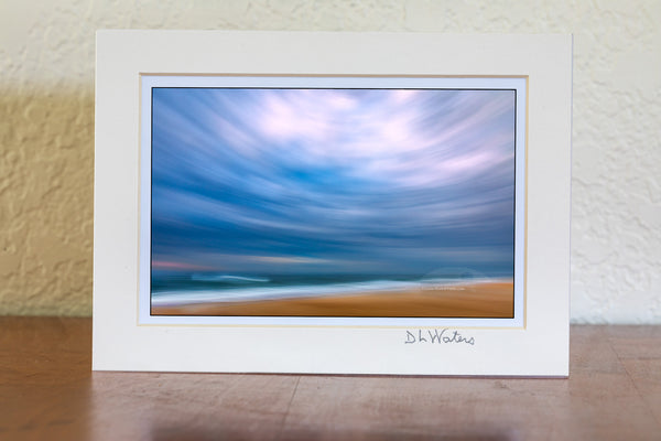 Using my wide-angle lens and tilting the camera up to include mostly sky I swung the camera down the beach keeping the horison level during the 1/10 of a second exposure. This camera technique is known as ICM photography or intentional camera movement photography. Distortion from tilting the 16 mm wide angle lens up created this circular affect. This photo was taken in the Cape Hatteras National Seashore in the Outer Banks of NC.