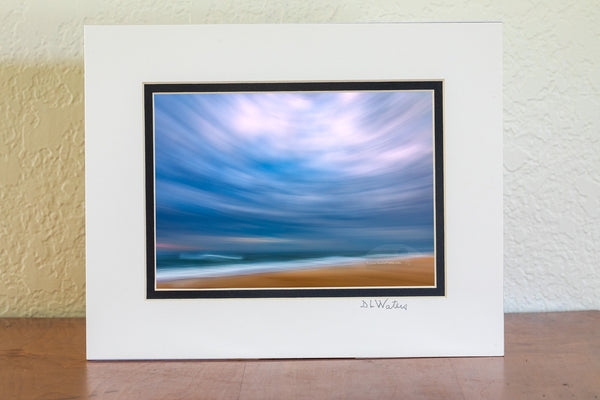 Using my wide-angle lens and tilting the camera up to include mostly sky I swung the camera down the beach keeping the horison level during the 1/10 of a second exposure. This camera technique is known as ICM photography or intentional camera movement photography. Distortion from tilting the 16 mm wide angle lens up created this circular affect. This photo was taken in the Cape Hatteras National Seashore in the Outer Banks of NC.