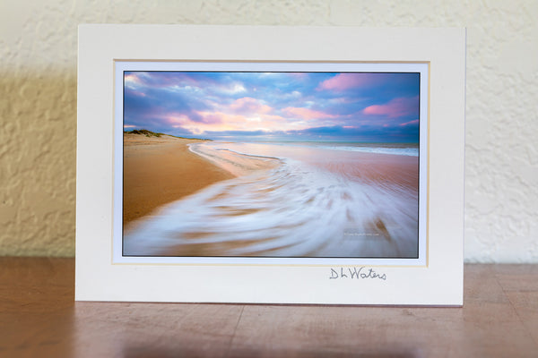 Sunrise with sweping wave at Cape Hatteras National Seashore on the Outer Banks, NC. While watching the waves ebb and flow I envisioned this photo. I knewI wanted the empty beach with the spectacular early morning light on the clouds as the sea foam swept back out to sea with a long enough shutter speed to show the motion.