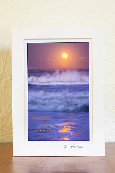 A nearly full moon photographed at twilight with a 1.3-second exposure beautifully captures the movement of the waves and the reflection of the moonlight in Kitty Hawk, located in the Outer Banks of North Carolina.