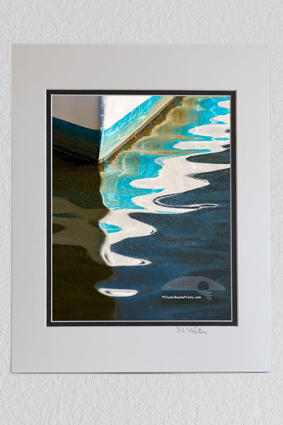 Pattern of light, shadow, and color in the reflection of the bow of a fishing boat in Wancheese Harbor on the Outer Banks of NC.