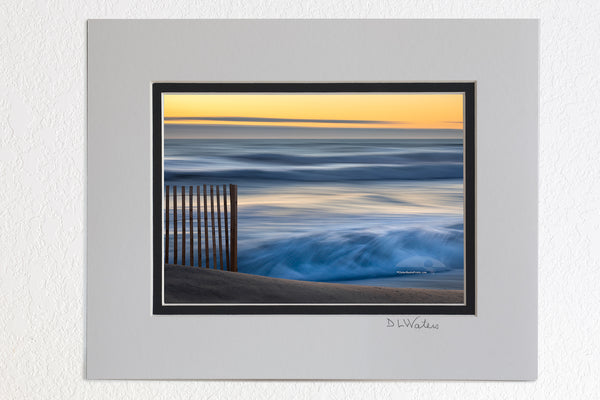 5 x 7 luster prints in a 8 x 10 ivory and black double mat of  This photo was taken with a heavy wind blowing the surf into a frenzy. There was no beach to walk on and every fifth wave came over the dune. The contrast between the foreground sand fence, and the moving waves in the background helps to convey a real sense of motion.