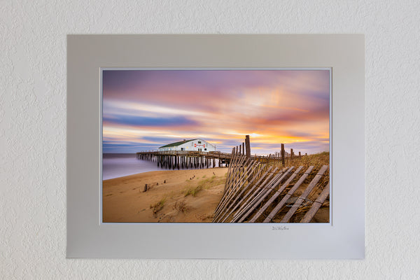 13 x 19 luster print in 18 x 24 ivory mat of Long exposure of sand fence, sunrise, clouds, and Kitty Hawk Fishing Pier on the Outer Banks of NC.