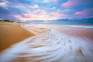 Sunrise with sweping wave at Cape Hatteras National Seashore on the Outer Banks, NC. While watching the waves ebb and flow I envisioned this photo. I knewI wanted the empty beach with the spectacular early morning light on the clouds as the sea foam swept back out to sea with a long enough shutter speed to show the motion.