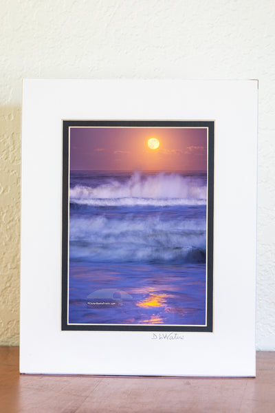 A nearly full moon photographed at twilight with a 1.3-second exposure beautifully captures the movement of the waves and the reflection of the moonlight in Kitty Hawk, located in the Outer Banks of North Carolina.