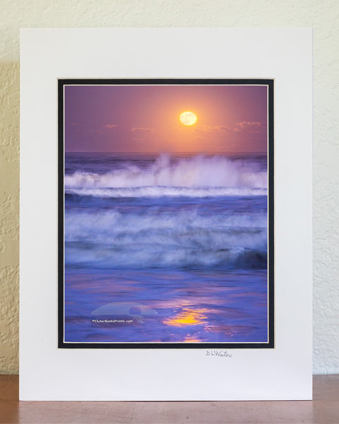 A nearly full moon photographed at twilight with a 1.3-second exposure beautifully captures the movement of the waves and the reflection of the moonlight in Kitty Hawk, located in the Outer Banks of North Carolina.