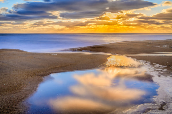 A tide pool at Kitty Hawk beach on the Outer Banks of NC reflecting a tranquil sunrise.