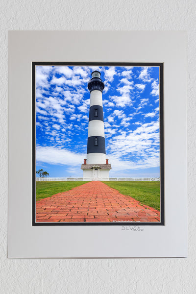 8 x 10 luster print in a 11 x 14 ivory and black double mat of Bodie Island Lighthouse red brick walkway leading up to the lighthouse and a blue sky with puffy white clouds.