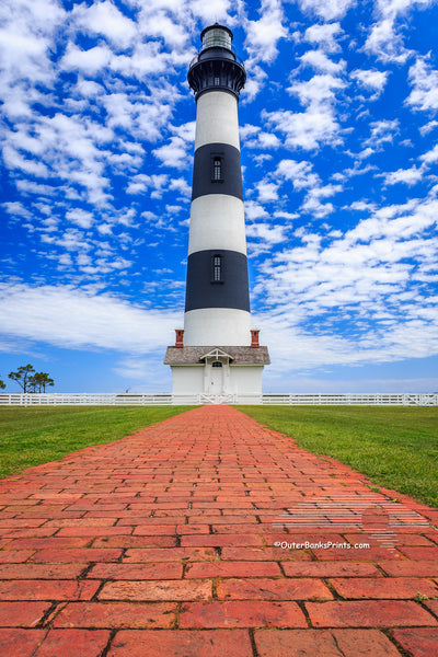 Bodie Island Lighthouse red brick walkway leading up to the lighthouse and a blue sky with puffy white clouds.