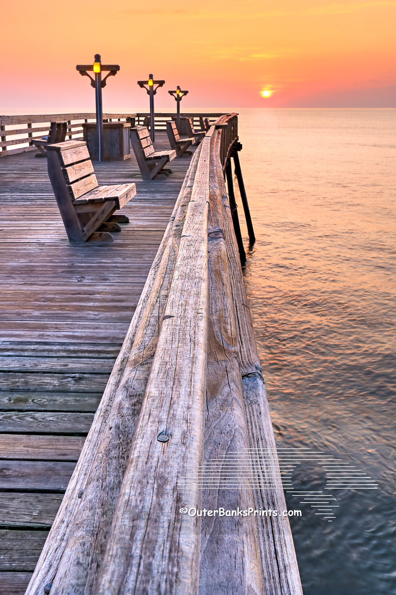 The railing of Kitty Hawk Fishing Pier leads to the sun breaking the horizon.