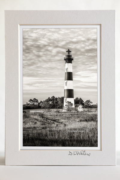 4 x 6 luster print in a 5 x 7 ivory mat of Black-and-white portrait of bodie Island Lighthouse. Bodie Island Lighthouse stands 156 feet tall and the height of each stripe is 22 feet. It is thought that the island got its name because of the many bodies that washed up from shipwrecks. The inside plaque reads, “Body Island”. no one is certain how the spelling change came about.