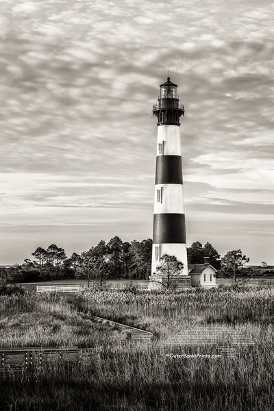 Black-and-white portrait of bodie Island Lighthouse. Bodie Island Lighthouse stands 156 feet tall and the height of each stripe is 22 feet. It is thought that the island got its name because of the many bodies that washed up from shipwrecks. The inside plaque reads, “Body Island”. no one is certain how the spelling change came about.