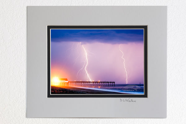 5 x 7 luster prints in a 8 x 10 ivory and black double mat of Lightning storm at Kitty Hawk Fishing Pier NC. The yellow light on the pier is a powerful street light shining on to the beach.