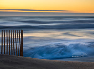 This photo was taken with a heavy wind blowing the surf into a frenzy. There was no beach to walk on and every fifth wave came over the dune. The contrast between the foreground sand fence,  and the moving waves in the background helps to convey a real sense of motion.