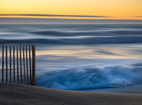 This photo was taken with a heavy wind blowing the surf into a frenzy. There was no beach to walk on and every fifth wave came over the dune. The contrast between the foreground sand fence,  and the moving waves in the background helps to convey a real sense of motion.