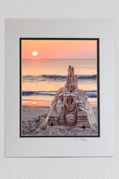 8 x 10 luster print in a 11 x 14 ivory and black double mat of The sun rises over an elaborate sand castle in Corolla on the Outer Banks NC.