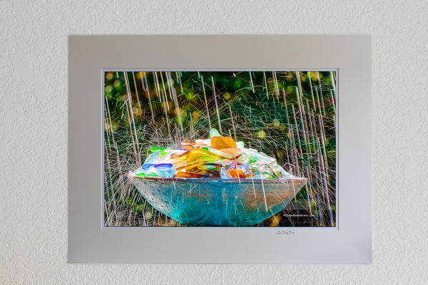 13 x 19 luster print in 18 x 24 ivory ￼￼mat of This beach glass was found on the beaches of the Outer Banks. It is just a small part of our collection. Broken bottles are smoothed and tumbled by the surf and sand before it becomes sea glass. I photographed this in my backyard using an oscillating sprinkler.The slow shutter speed and back light made of the sprinkler look like raindrops.