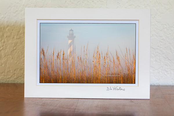 Cape Hatteras lighthouse in the fog behind a line of sea oats in the sun at Buxton North Carolina in Cape Hatteras National Seashore.