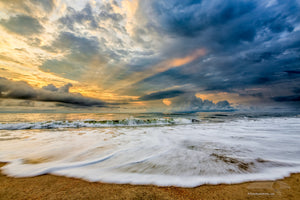 Sunrise and clouds with light rays poking through stormy skies over Kill Devil Hills beach on the Outer Banks of NC.
