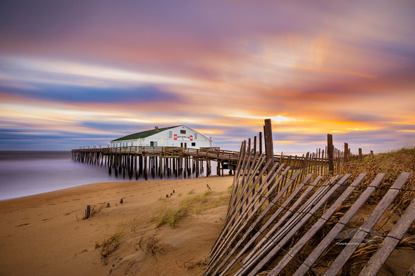 Long exposure of sand fence, sunrise, clouds, and Kitty Hawk Fishing Pier on the Outer Banks of NC.