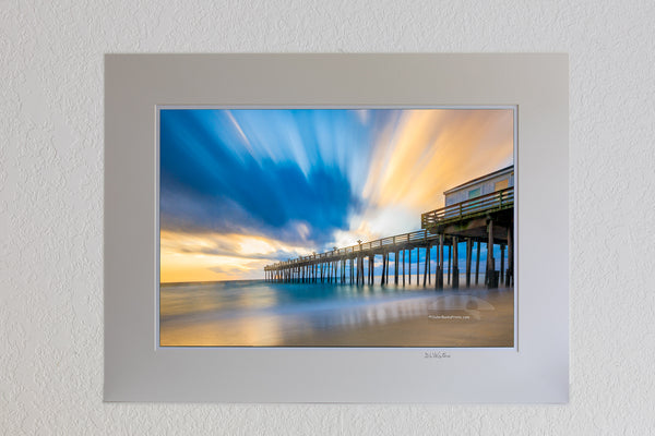13 x 19 luster print in 18 x 24 ivory ￼￼mat of Long exposure showing the motion of the clouds and surf at Kitty Hawk Fishing Pier sunrise on the Outer Banks of NC.