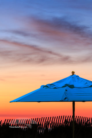 A lone beach umbrella left up from the day before, photographed on Kitty Hawk beach at sunrise.￼￼￼￼ I used a flashlight during a long exposure￼ to light-paint the backlit ￼umbrella so it would not be a silhouette￼. The flashlight has to be moved constantly to evenly light the￼ subject while light painting.￼￼￼