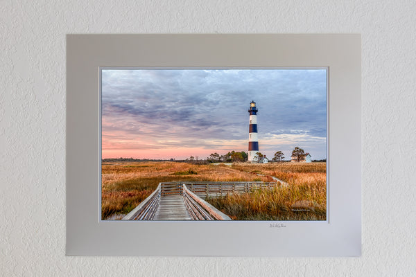 13 x 19 luster print in 18 x 24 ivory ￼￼mat of A walkway through the marsh leading to Bodie Island Lighthouse at sunrise.
