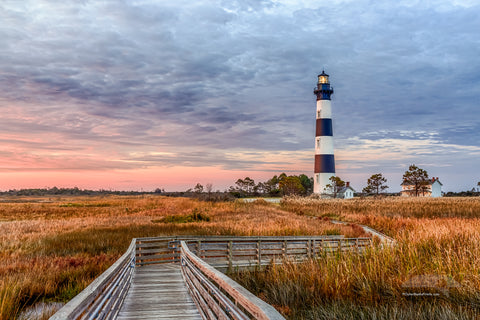 A walkway through the marsh leading to Bodie Island Lighthouse at sunrise.